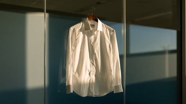 Single pressed white dress shirt on a hanger against a glass office wall